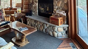 L’intérieur d’un chalet accueillant, avec une cheminée en pierre, un plafond en bois et une grande fenêtre.