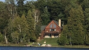 Une cabane dotée d’une grande cheminée, entourée d’une forêt dense et bordée d’un lac.