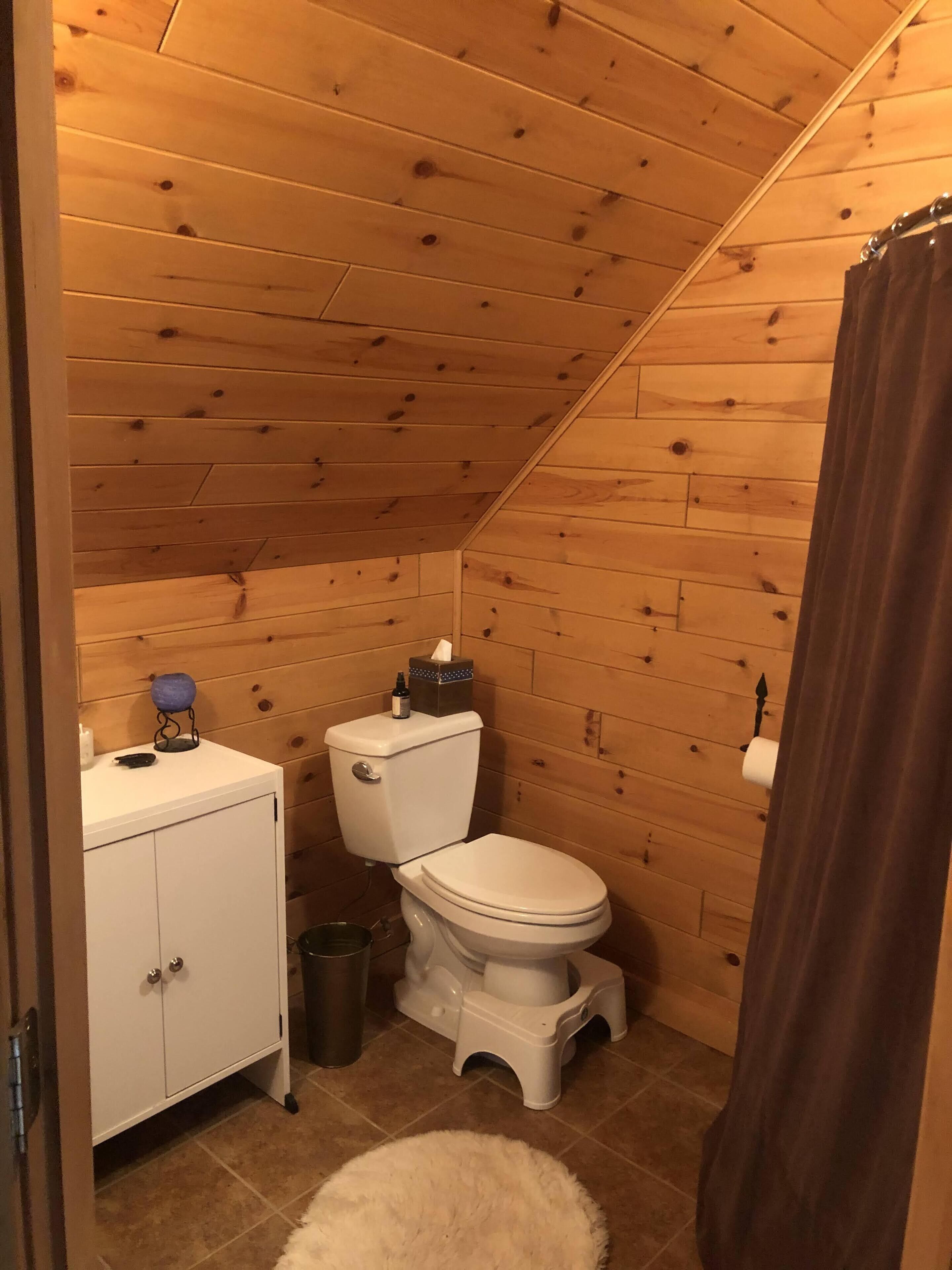 A small, wooden-paneled bathroom with a toilet, a cabinet, and a trash can.
