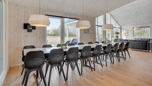 Un comedor amplio con una larga mesa y sillas, ventanas grandes e iluminación colgante.