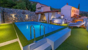 A swimming pool with a stone wall and a white building with a balcony in the background. - Beautiful home in Tribalj with sauna (Tribalj)