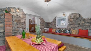 A rustic stone-walled room with a wooden table set for a meal, a bench with cushions, and a stone fireplace. - Beautiful home in Tribalj with sauna (Tribalj)