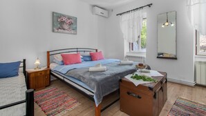 A bedroom with a bed, bedside table, lamp, air conditioning unit, window with curtains, and a mirror. - Beautiful home in Tribalj with sauna (Tribalj)