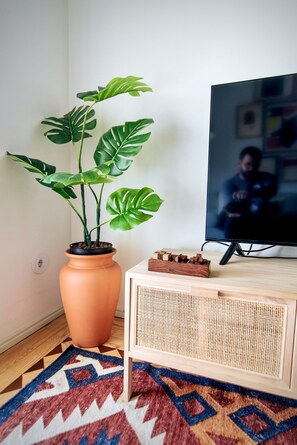 A room with a large potted monstera plant, a television, and a wooden console table. - Cidade D' Água—Queen-Size Bed & Private Patio (Almada)