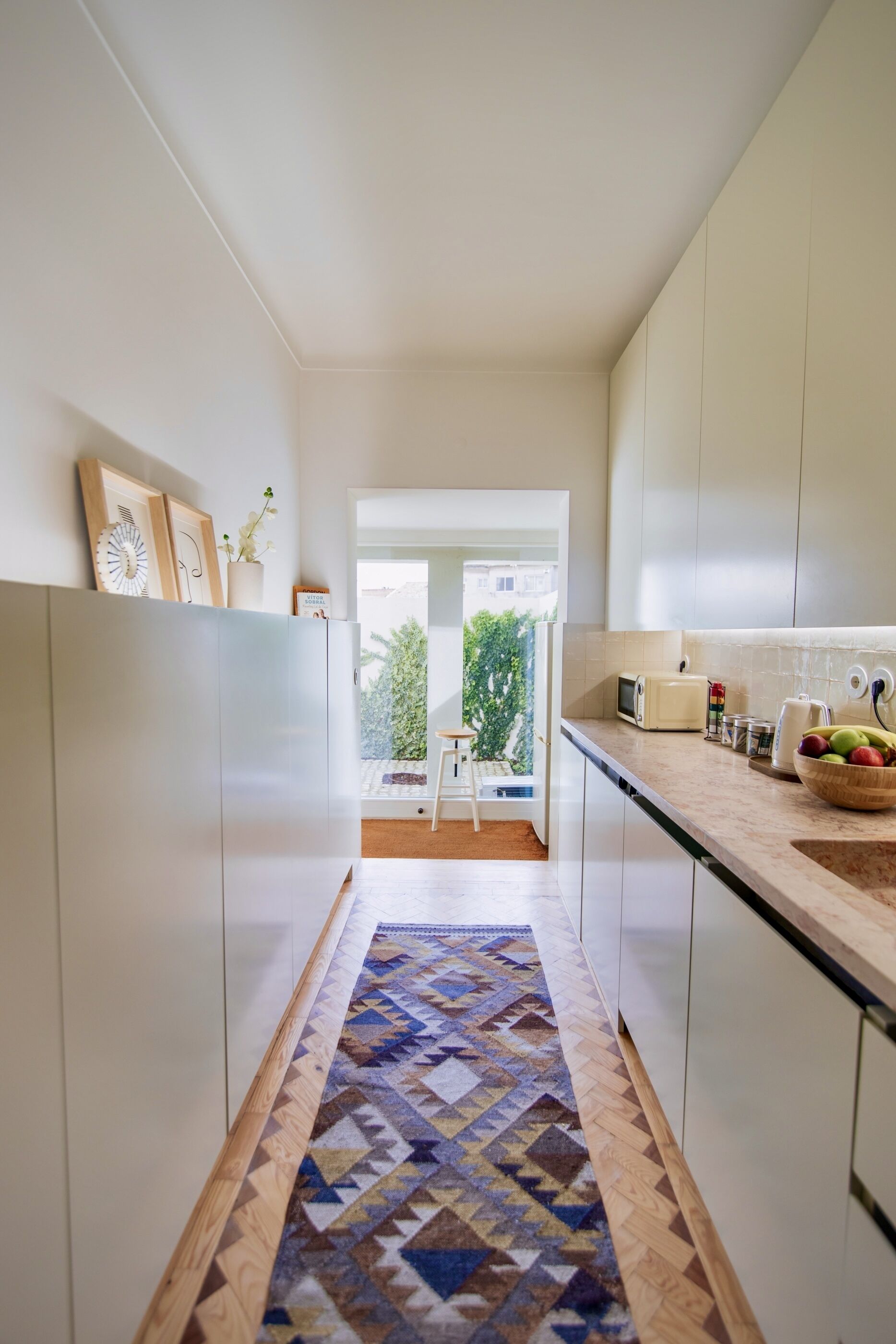 A modern kitchen with white cabinets, a patterned rug, and a view to an outdoor area.