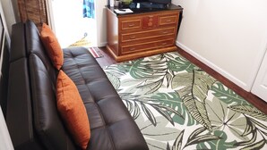 Un salon comprenant un canapé, une commode en bois, un téléviseur et un tapis à motifs.