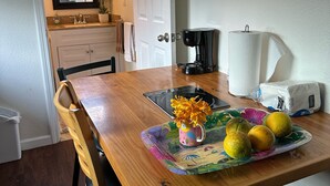 Une table à manger en bois, avec une machine à café, une assiette de citrons et un vase rempli de fleurs.