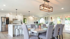 Une cuisine moderne avec des meubles blancs, un îlot central et un coin repas doté de chaises grises recouvertes de tissu.