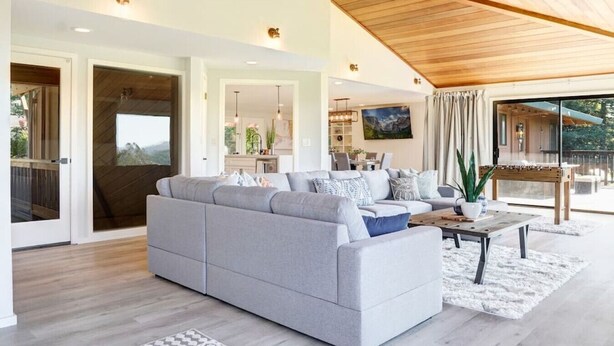 Un salon spacieux avec un canapé d’angle gris, un plancher en bois et un plafond en bois.