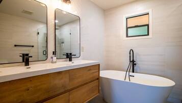 Ein modernes Badezimmer mit freistehender Badewanne, einem großen, beleuchteten Spiegel und einem Holzbadezimmer-Möbel.