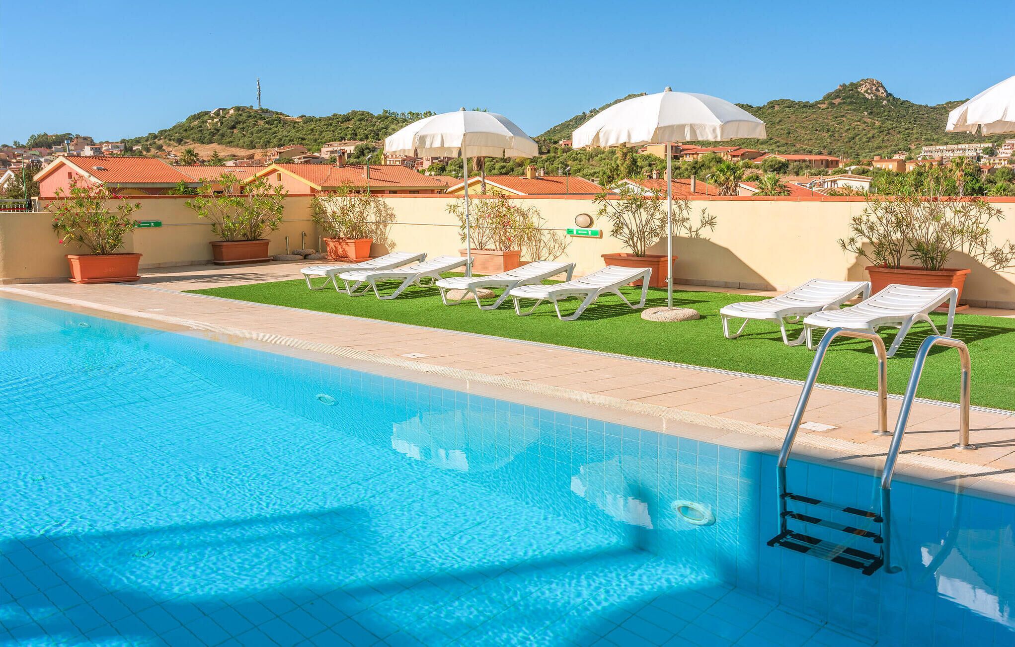 Une piscine entourée de chaises longues et de parasols, agrémentée de plantes en pot et offrant une vue sur une colline.