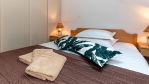 A neatly made bed with a brown headboard, white bedding, and a green leaf-patterned pillow. There are two bedside lamps with lampshades, and a folded beige towel on the bed. - 2 bedroom gorgeous home in Blace (Blace)