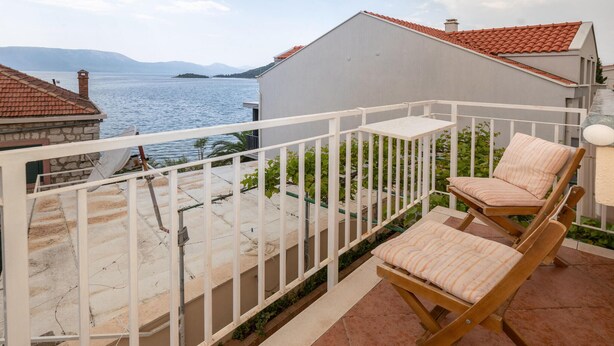A balcony with a white railing, two wooden chairs with striped cushions, and a view of the sea and distant hills. - 2 bedroom gorgeous home in Blace (Blace)