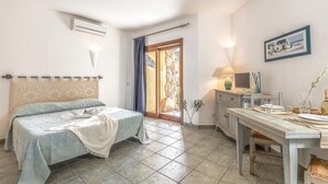 Un dormitorio con cama, escritorio, silla, lámpara y un cuadro en la pared.