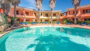 Una piscina rodeada de palmeras y un edificio con balcones.