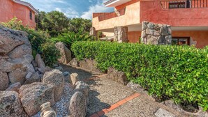 Un patio con un sendero de piedra, setos verdes y un edificio con un balcón.