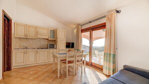 Et kompakt køkken med spiseplads, en sofa og en balkon med udsigt.