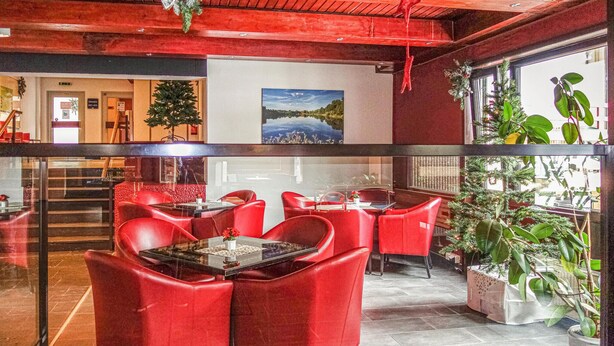 Un restaurant avec des chaises et des tables rouges, un sapin de Noël et un tableau représentant un lac.