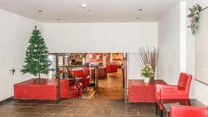 Un hall d’entrée avec un comptoir de réception, des sièges rouges, un sapin de Noël et, au fond, un coin cuisine.
