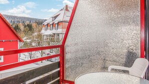 Un balcon avec une balustrade rouge, une table en verre et une chaise blanche.