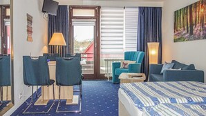 Une chambre d’hôtel avec un lit, deux chaises, un canapé, une télévision et une fenêtre avec des rideaux.