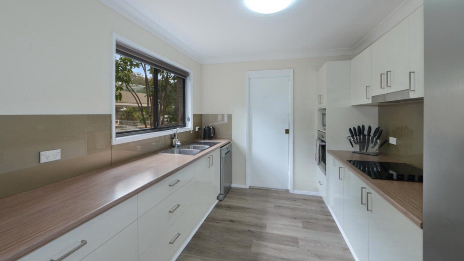 A modern kitchen with white cabinets, a wooden countertop, a window, and a door.