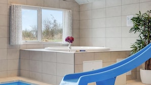 A modern bathroom with a bathtub, a blue slide, and a window with curtains. - Gorgeous home in Sydals with sauna (Sydals)