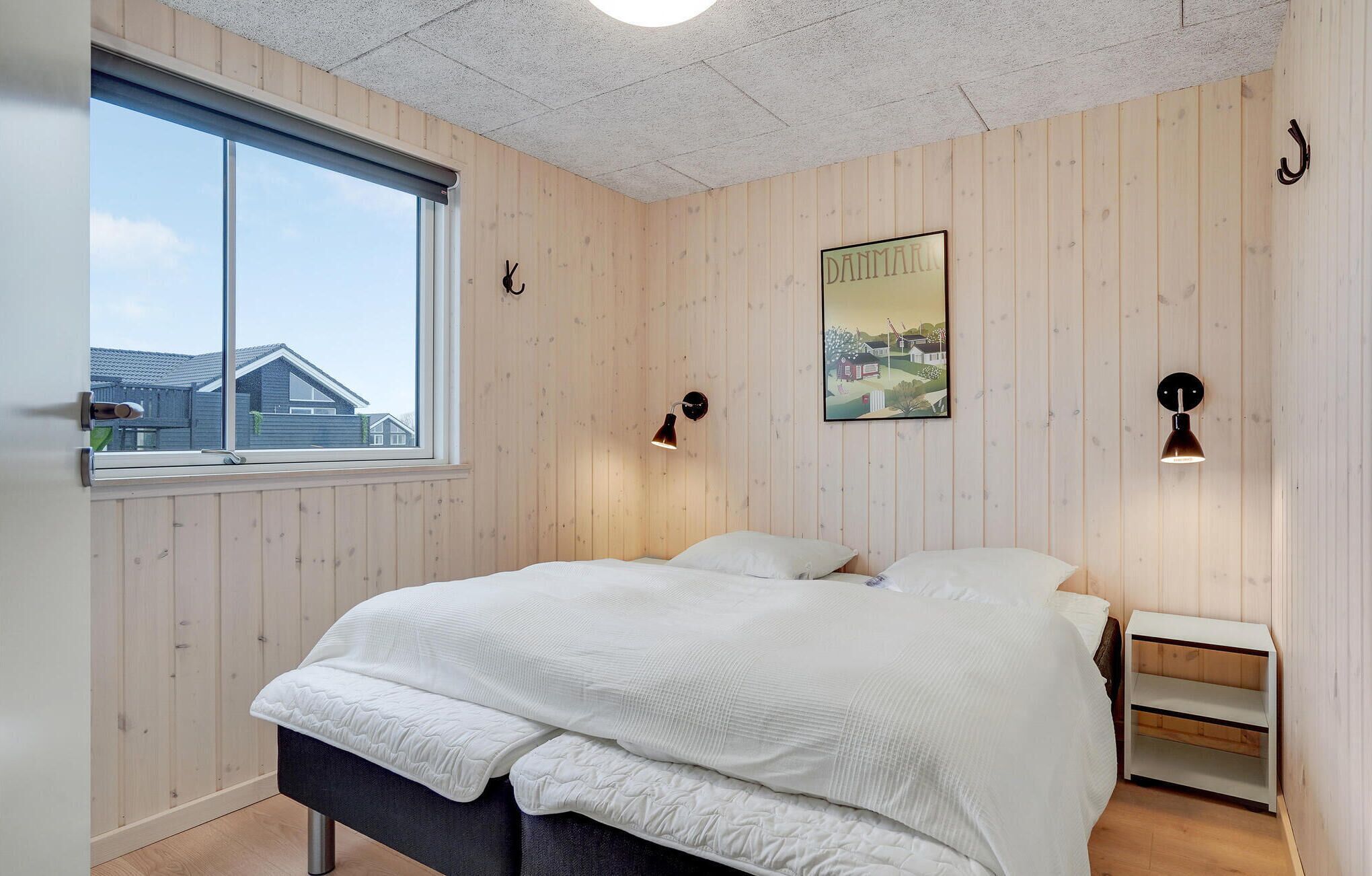 A bedroom with a large bed, wooden walls, a window, and two wall-mounted lamps.