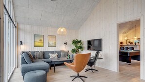 A modern living room with a grey sofa, a brown chair, a dining table, and a TV mounted on the wall. - Gorgeous home in Sydals with sauna (Sydals)