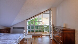 Ein Schlafzimmer mit einem großen Schiebeglastür, die auf einen Balkon führt, einem Bett, einem Sessel und einer Kommode.