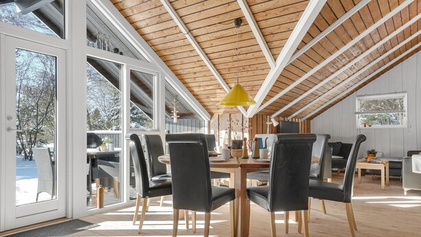 En rummelig spiseplads med højt til loftet og store vinduer, trægulv og moderne møbler.