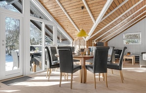 Une salle à manger spacieuse avec un plafond haut et de grandes fenêtres, un plancher en bois et un mobilier moderne.