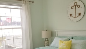 Un dormitorio con cama, ventilador de techo, ventana con cortinas, lámpara y decoración en la pared.
