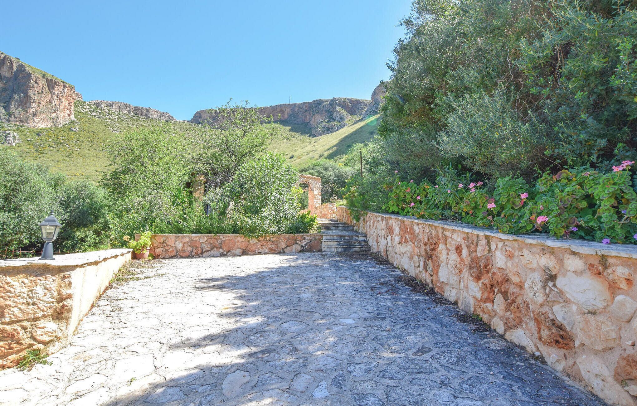 A stone pathway leading uphill, surrounded by greenery and a stone wall.