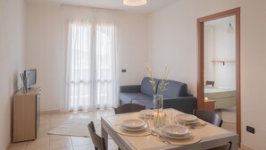 Un comedor con una mesa dispuesta para cuatro personas, un sofá, un televisor y un espejo.