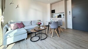A modern living room with a grey sofa, a round coffee table, and a kitchen area with cabinets and appliances.