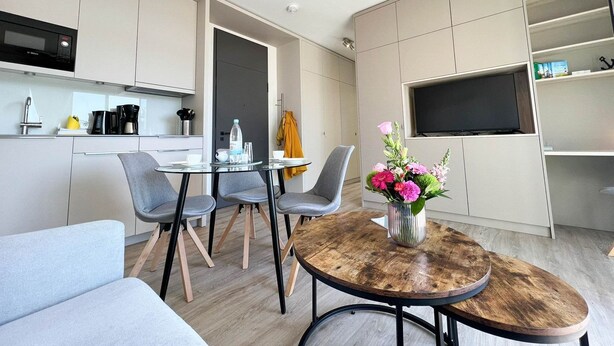 A modern, compact living space with a kitchenette, a dining area with a glass table, and a seating area with a sofa and chairs.