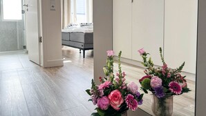 A bedroom with a bed, a dresser, and a mirror reflecting a hallway with a door and a window.