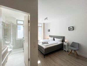 Ein modernes Schlafzimmer mit einem großen Bett, Nachttischen, einem Sessel und einer Dusche.