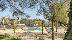 Columpios tipo hamaca en un parque con una piscina y un edificio al fondo.