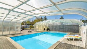 Una piscina techada con techo de vidrio, sillas de descanso y una pared de piedra.