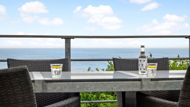 A dining area with a view of the sea, featuring a table with chairs and a bottle of water. - 2 bedroom gorgeous home in Gudhjem (Gudhjem)