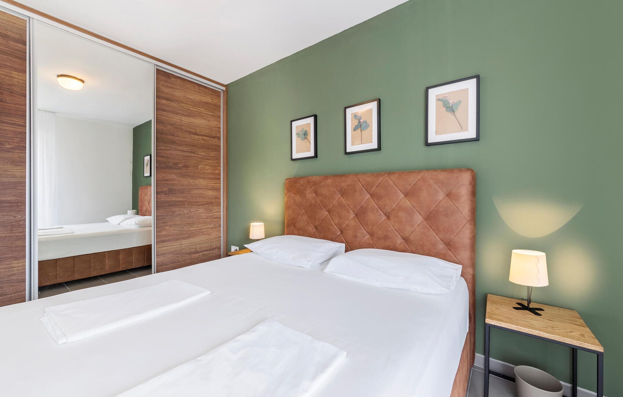 A hotel room with a large bed, a wooden headboard, a nightstand with a lamp, and a mirror.