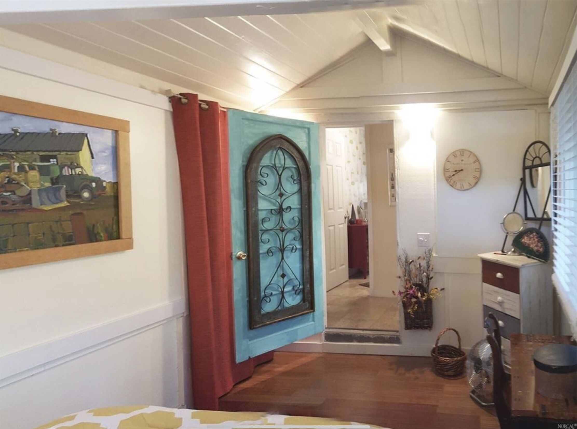 A hallway with a door featuring a decorative metal design, a framed picture on the wall, a clock, and a mirror.