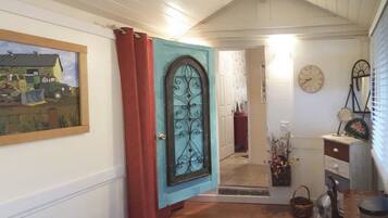A hallway with a door featuring a decorative metal design, a framed picture on the wall, a clock, and a mirror.