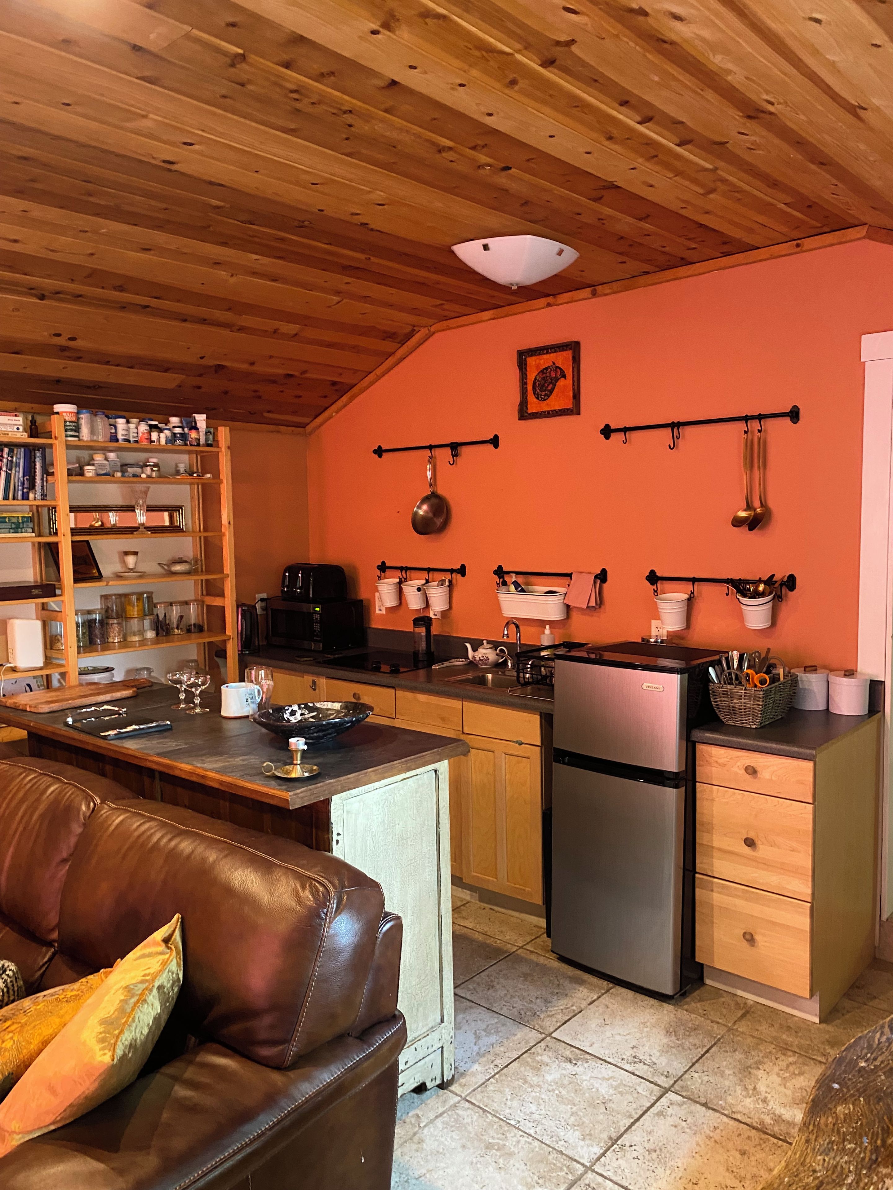 Une cuisine compacte avec des meubles en bois, un réfrigérateur et un coin repas agrémenté d’un canapé en cuir.