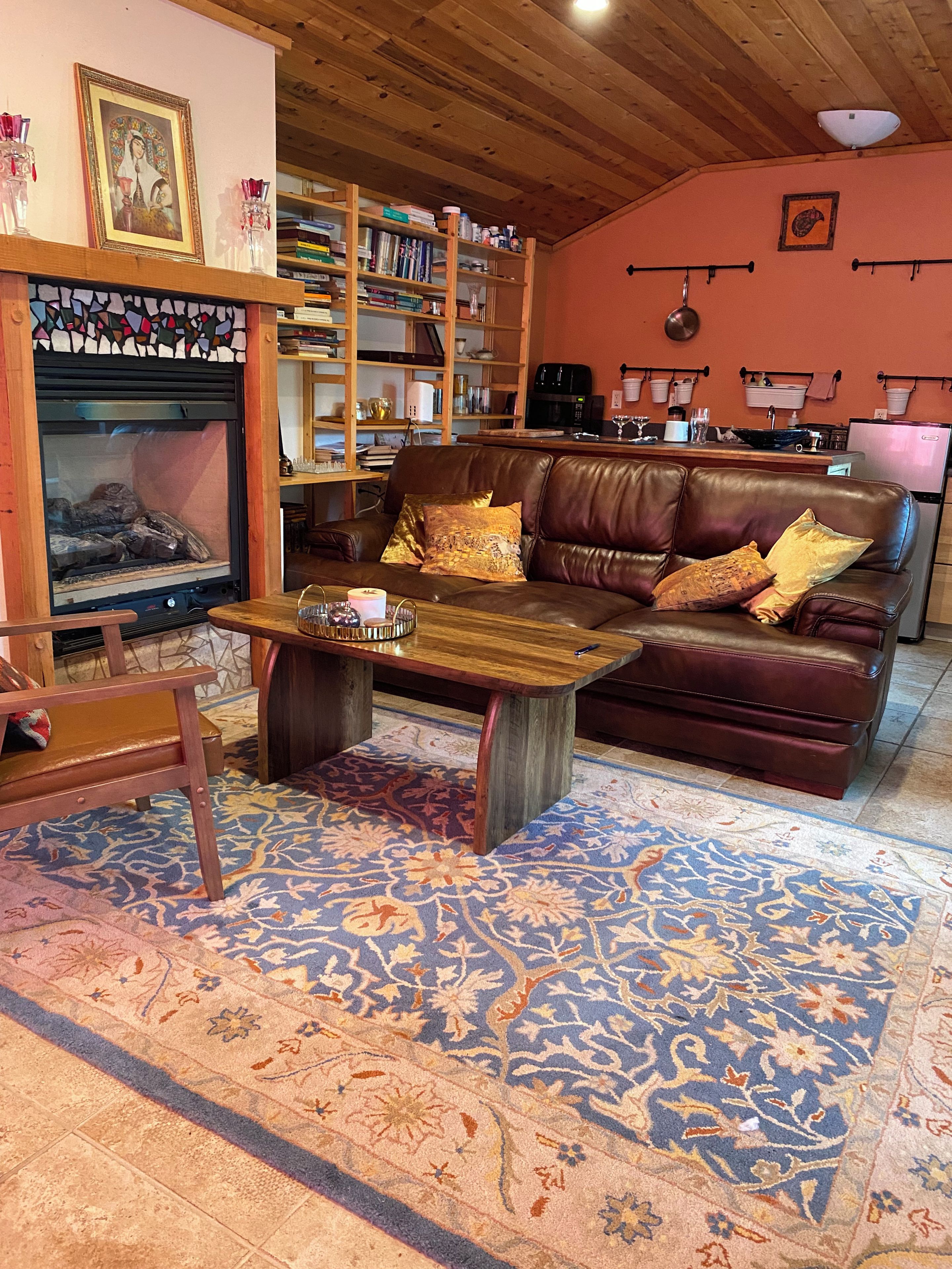 Un salon chaleureux avec une cheminée, un canapé en cuir, une table basse en bois et un tapis à motifs.