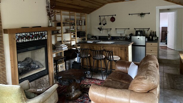 Una sala de estar acogedora con chimenea, techo de madera y una zona de cocina con refrigerador y fregadero.