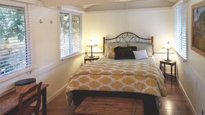 Un dormitorio con una cama, dos mesitas de noche, una silla y una ventana con persianas.