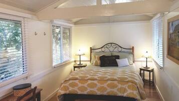 A bedroom with a bed, two bedside tables, a chair, and a window with blinds.
